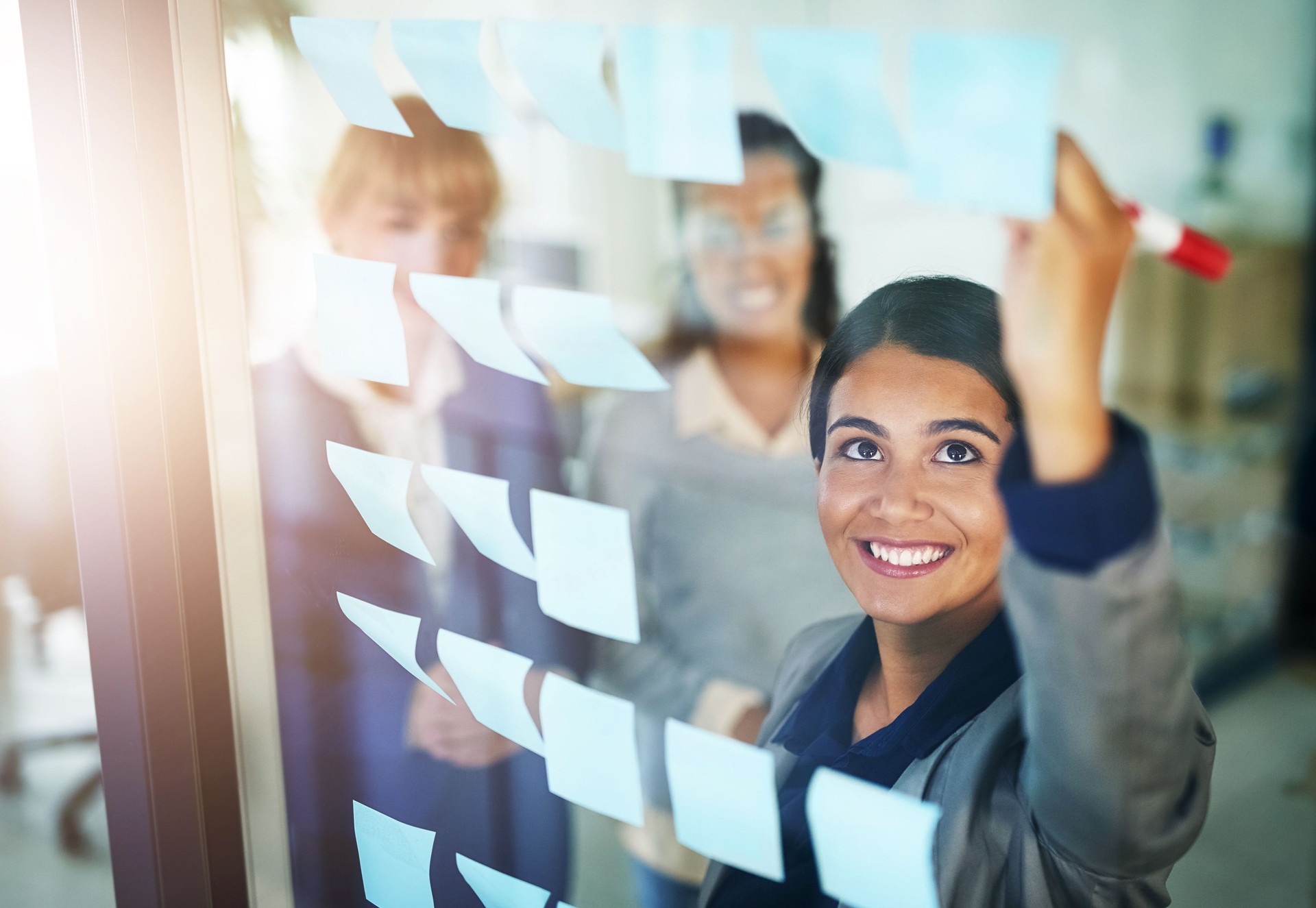 Business people, teamwork or happy woman writing on board for brainstorming a solution, ideas or goals. Planning, sticky note or creative group with leadership for project collaboration together