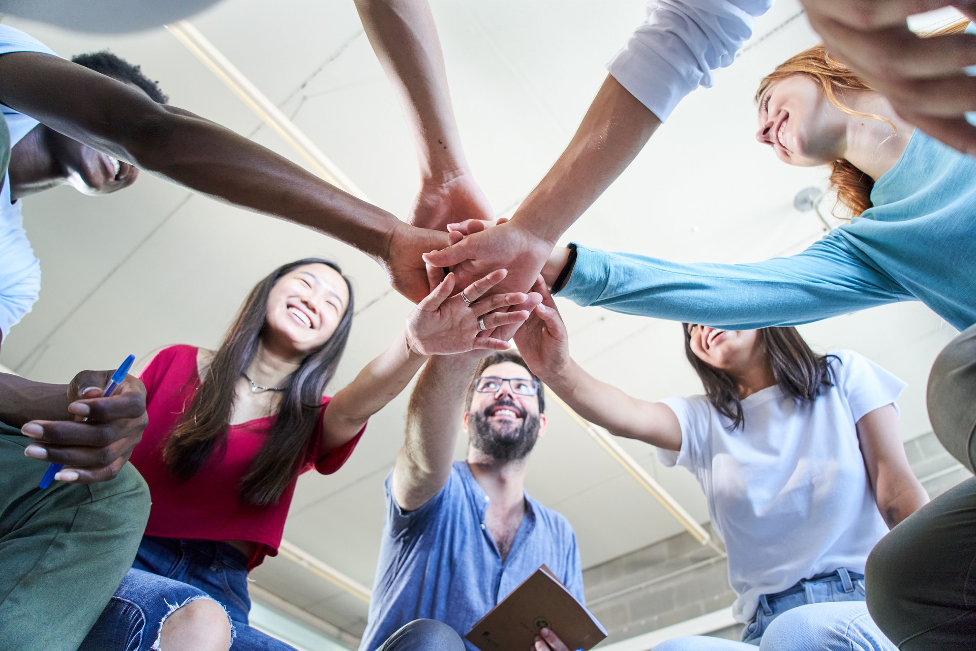 Low angle view of a group of happy young students with teacher stacking hands hands .